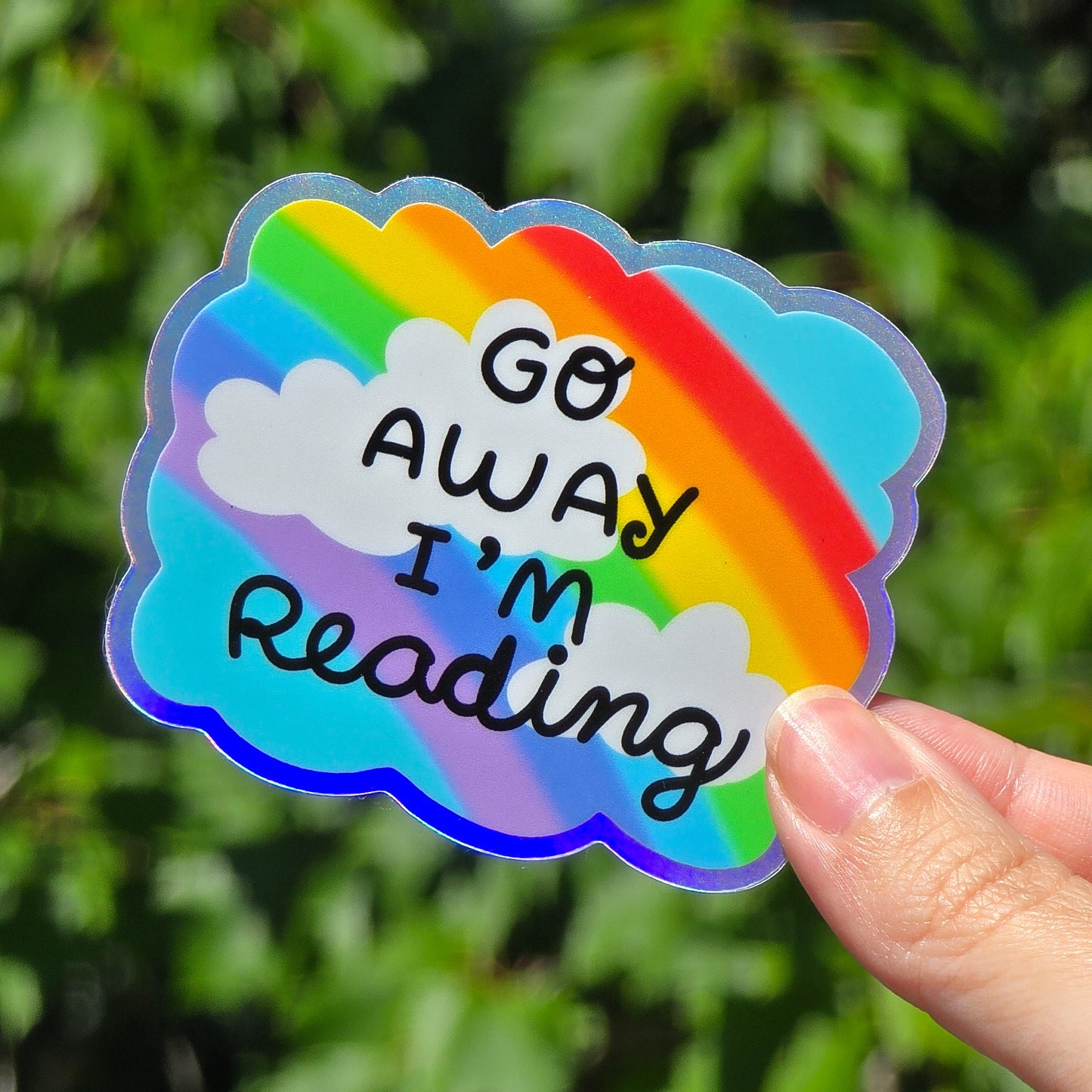 rainbow against a blue sky with clouds. it says go away i'm reading in black font. holographic border all around