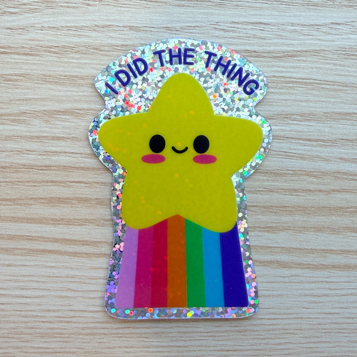 Star-shaped sticker with rainbow colors and 'I DID THE THING' text on a wooden surface