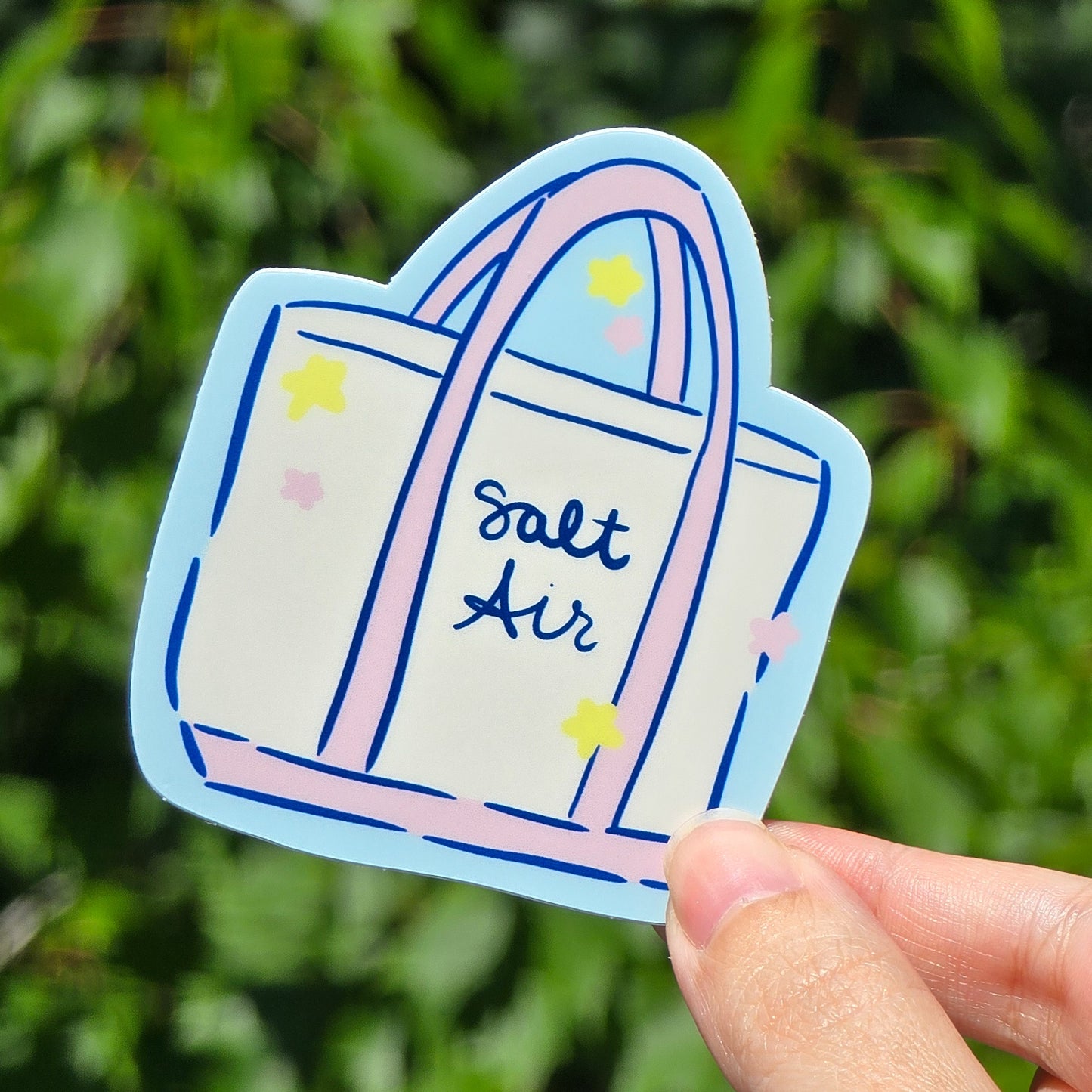 sticker of a tote bag that says salt air. it is a white bag with pink trim and handles