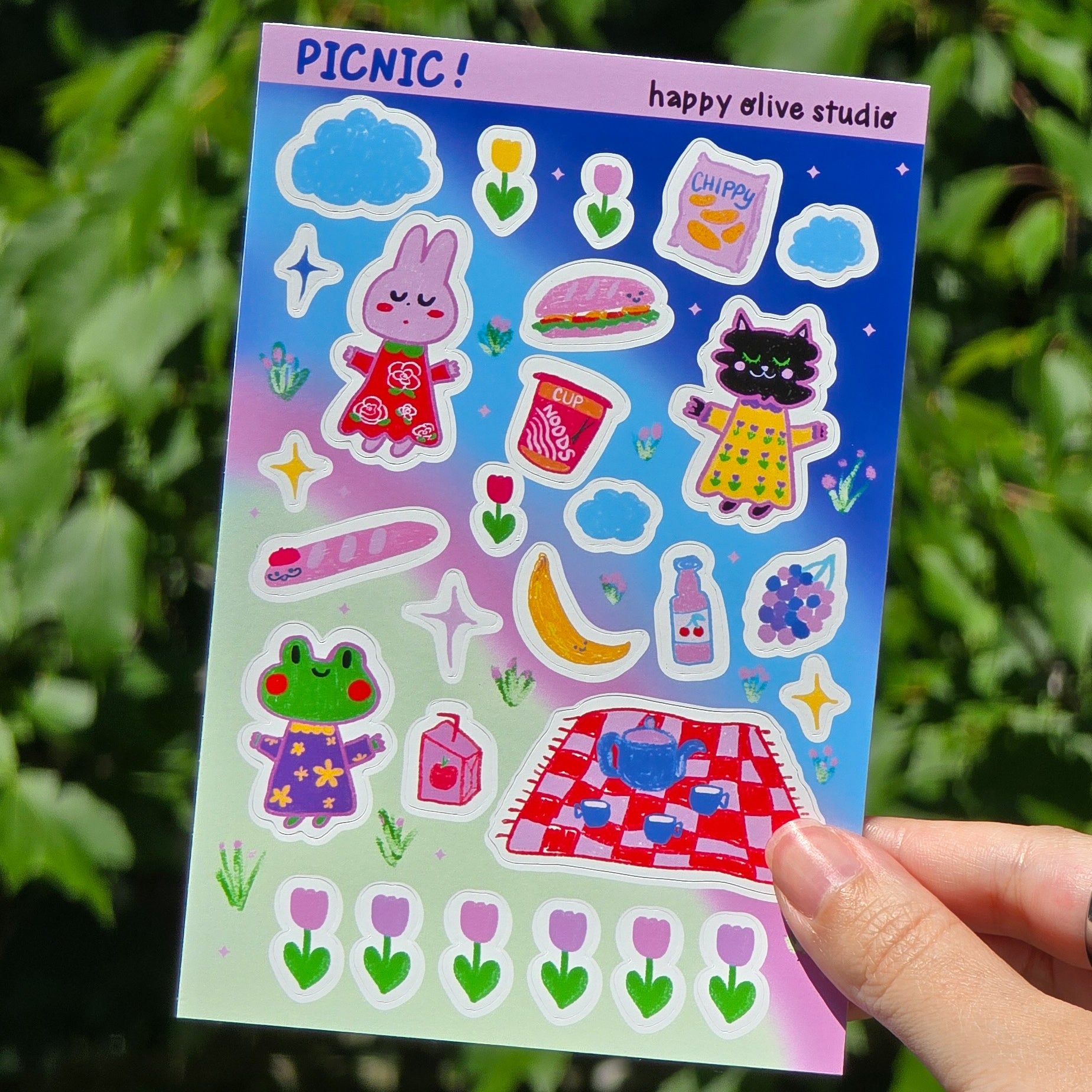 sticker sheet featuring picnic foods, a bunny, cat, and frog against a blue pink and green background. there are flowers and clouds and stars too
