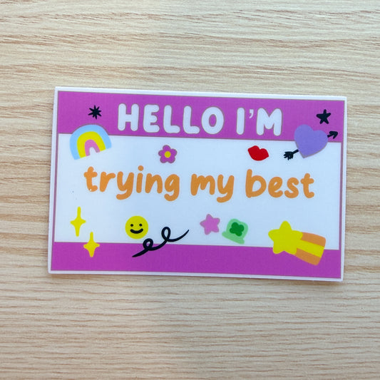 Colorful name tag sticker with 'Hello I'm trying my best' text on a wooden surface