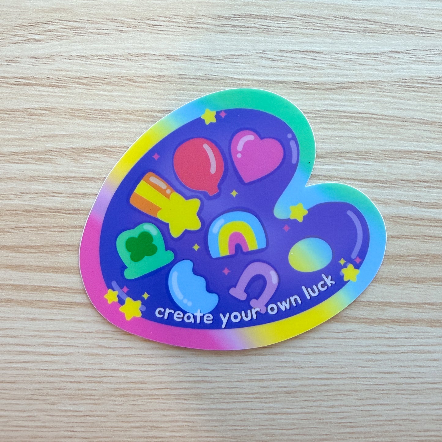Colorful sticker with various symbols and 'create your own luck' text on a wooden surface