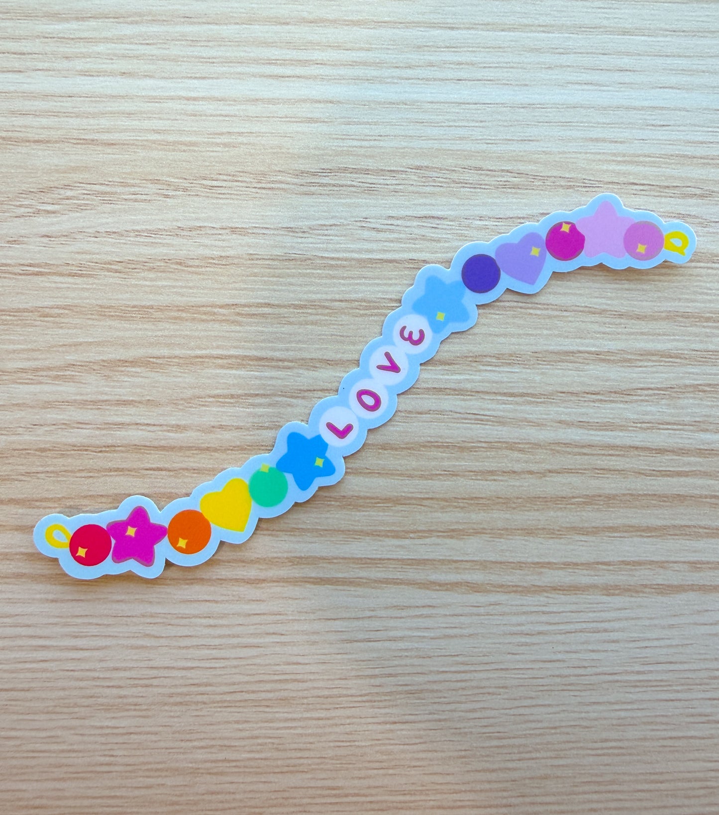 Colorful 'LOVE' sticker on a wooden surface in the shape of a long beaded bracelet