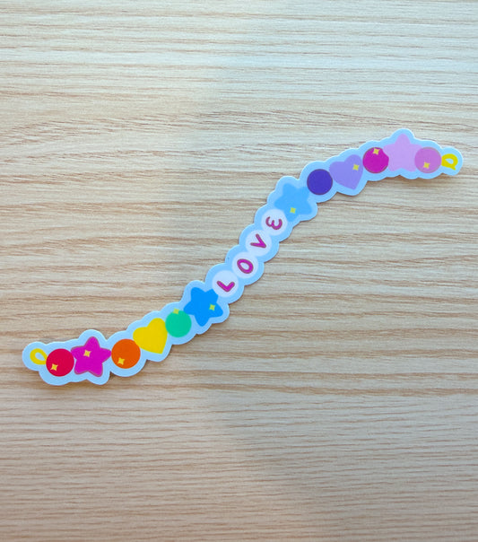 Colorful 'LOVE' sticker on a wooden surface in the shape of a long beaded bracelet