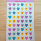 Sheet of colorful heart-shaped letter stickers with 'happy olive studio' branding on a wooden surface.